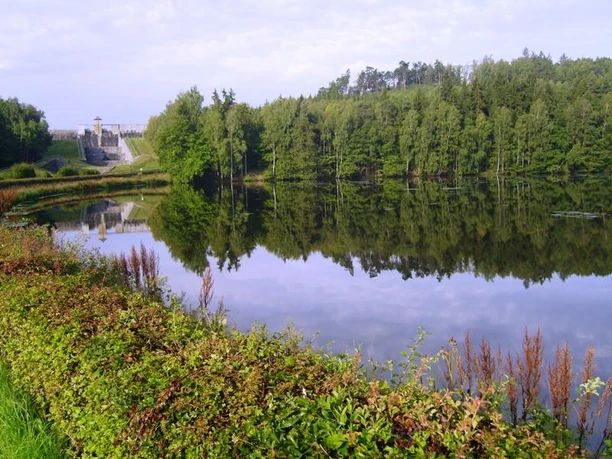 A tranquil lake with a wooded shoreline, aspired by a small dam under a blue sky.