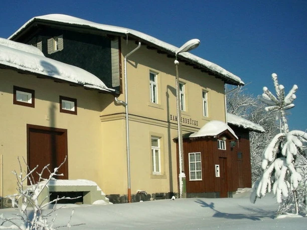 Snow-covered building in front of a clear blue sky, surrounded by snow-covered trees.