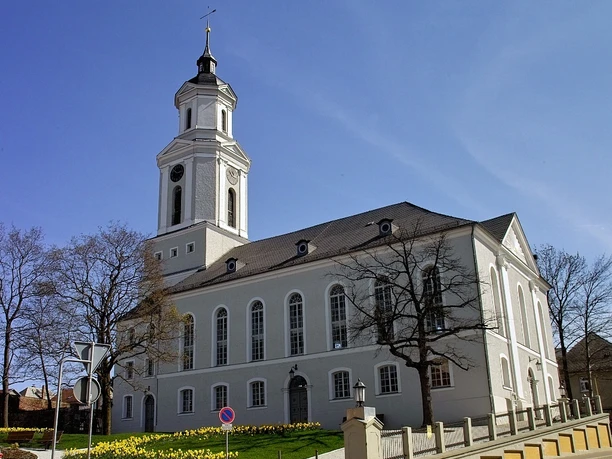 Dreieinigkeitskirche Zeulenroda Dreieinigkeitskirche in Zeulenroda, Barockarchitektur mit weißem Turm und blühenden Blumen im Vordergrund.