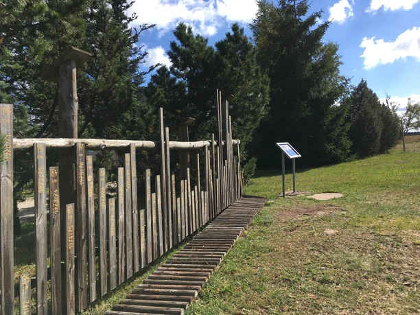 Ski day fence in Zinnwald made of wooden poles with explanatory boards, surrounded by green trees.