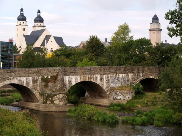 Alte Elsterbrücke Steinerne Bogenbrücke über Fluss, im Hintergrund historische Gebäude mit Türmen.