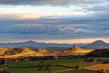 Uitgestrekt landschap met heuvels en een indrukwekkende rots in het midden, wolken erboven.