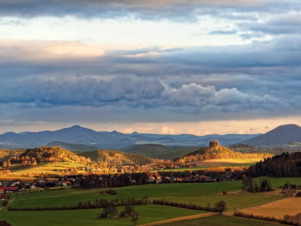 Extensive landscape with hills and an impressive rock in the middle, clouds above.