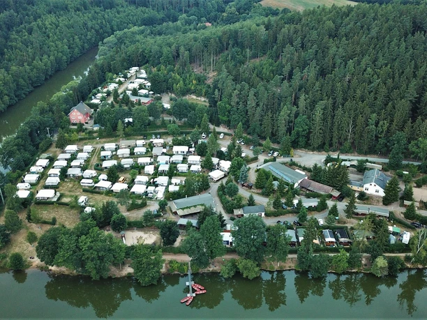 Naturcampingplatz Weida Luftaufnahme eines Naturcampingplatzes am Waldrand mit vielen Wohnwagen entlang eines Flusses.