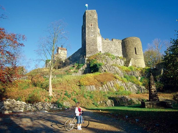 Mighty Stolpen Castle on a rocky hill, surrounded by autumn foliage and cyclists in the foreground.