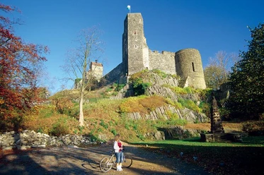 Burg Stolpen Mächtige Burg Stolpen auf felsiger Anhöhe, umgeben von herbstlichem Laub und Radfahrer im Vordergrund.
