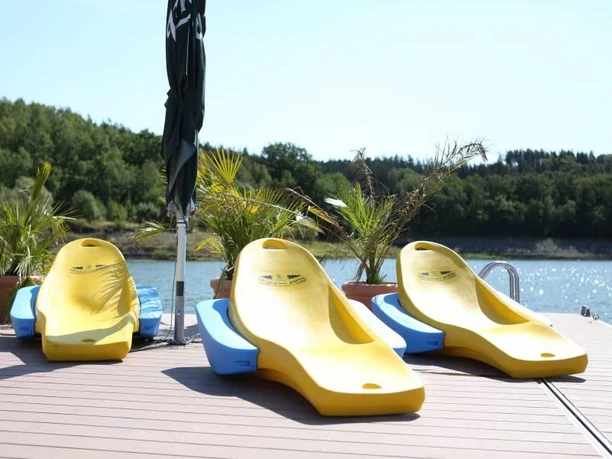 Three yellow water slides on a jetty in front of a lake, surrounded by a green landscape.