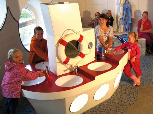 Campingplatz LuxOase Kinderwaschland Kinderwaschland mit maritimer Gestaltung, fröhliche Kinder beim Spielen und Händewaschen.