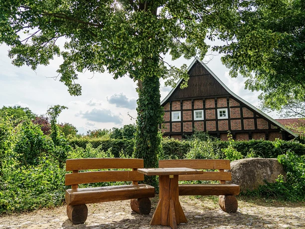 Nortrup in het Artland Houten bank en tafel in de schaduw van grote bomen voor een vakwerkhuis op een zonnige dag.