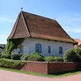 Alte Kapelle in Haßbergen mit rotem Ziegeldach, weißen Mauern und umgeben von grüner Hecke.