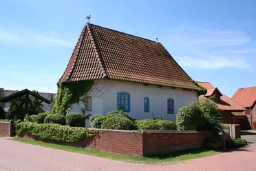 Alte Kapelle Haßbergen Alte Kapelle in Haßbergen mit rotem Ziegeldach, weißen Mauern und umgeben von grüner Hecke.