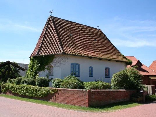 Alte Kapelle Haßbergen Alte Kapelle in Haßbergen mit rotem Ziegeldach, weißen Mauern und umgeben von grüner Hecke.