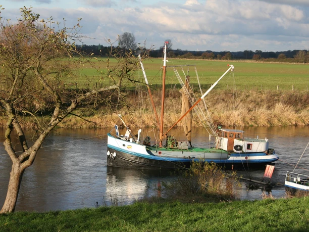 Aalschokker on the Weser off Drakenburg, surrounded by meadows and a cloudy sky.