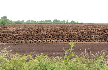 Lichtenmoor Torfstapel in einem ausgedehnten und flachen Landschaftsbereich, umgeben von Vegetation und bewölktem Himmel.