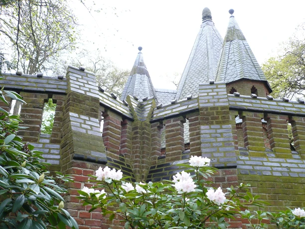 Brick mausoleum with tiled pointed roofs in front of blooming rhododendrons in the castle park.