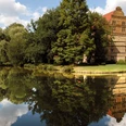 Wasserschloß Holtfeld Historisches Haus mit rotem Dach und Bäumen spiegelt sich idyllisch in einem ruhigen Teich wider.