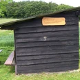 Schutzhütte Hummerser Busch Holzhütte mit Flachdach auf Wiese vor Wald und Feldern; Tisch-Bank-Kombination daneben.