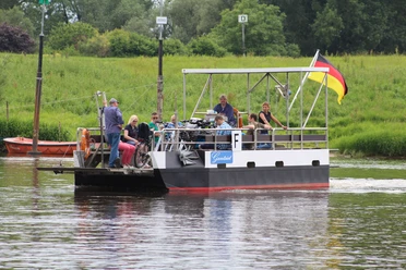 Weserfähre transportiert Personen und Fahrräder über einen ruhigen Fluss vor grüner Landschaft.