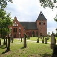 St.-Sigismund-Kirche in Daverden, Backsteingotik mit Friedhof, umgeben von Bäumen, unter blauem Himmel.