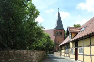 St. Laurentius-Kirche Liebenau Straße führt zu einer historischen Backsteinkirche mit spitzem Turm, flankiert von Fachwerkhäusern.
