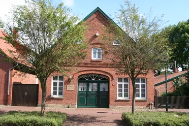 Witten Hus Liebenau Backsteinhaus mit grünen Doppeltüren, weißen Fenstern und einladender Fassade, flankiert von Bäumen.
