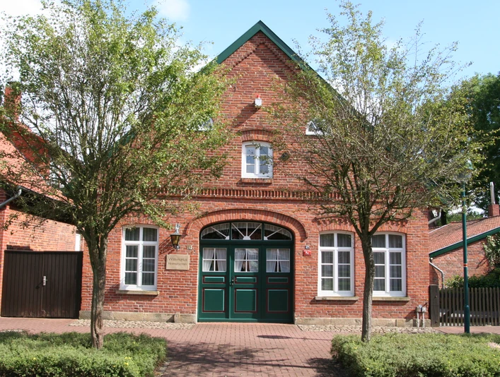 Witten Hus Liebenau Backsteinhaus mit grünen Doppeltüren, weißen Fenstern und einladender Fassade, flankiert von Bäumen.
