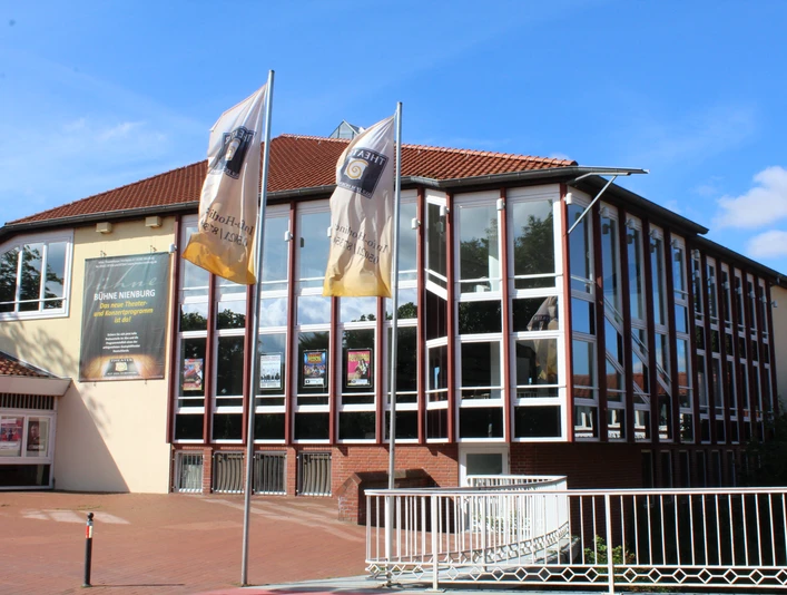 Kulturzentrum mit markanten Glasfassaden und Wimpel vorm Haupteingang, blauer Himmel im Hintergrund.