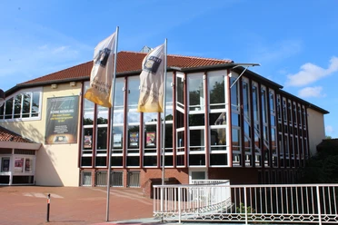 Theater auf dem Hornwerk Nienburg Kulturzentrum mit markanten Glasfassaden und Wimpel vorm Haupteingang, blauer Himmel im Hintergrund.