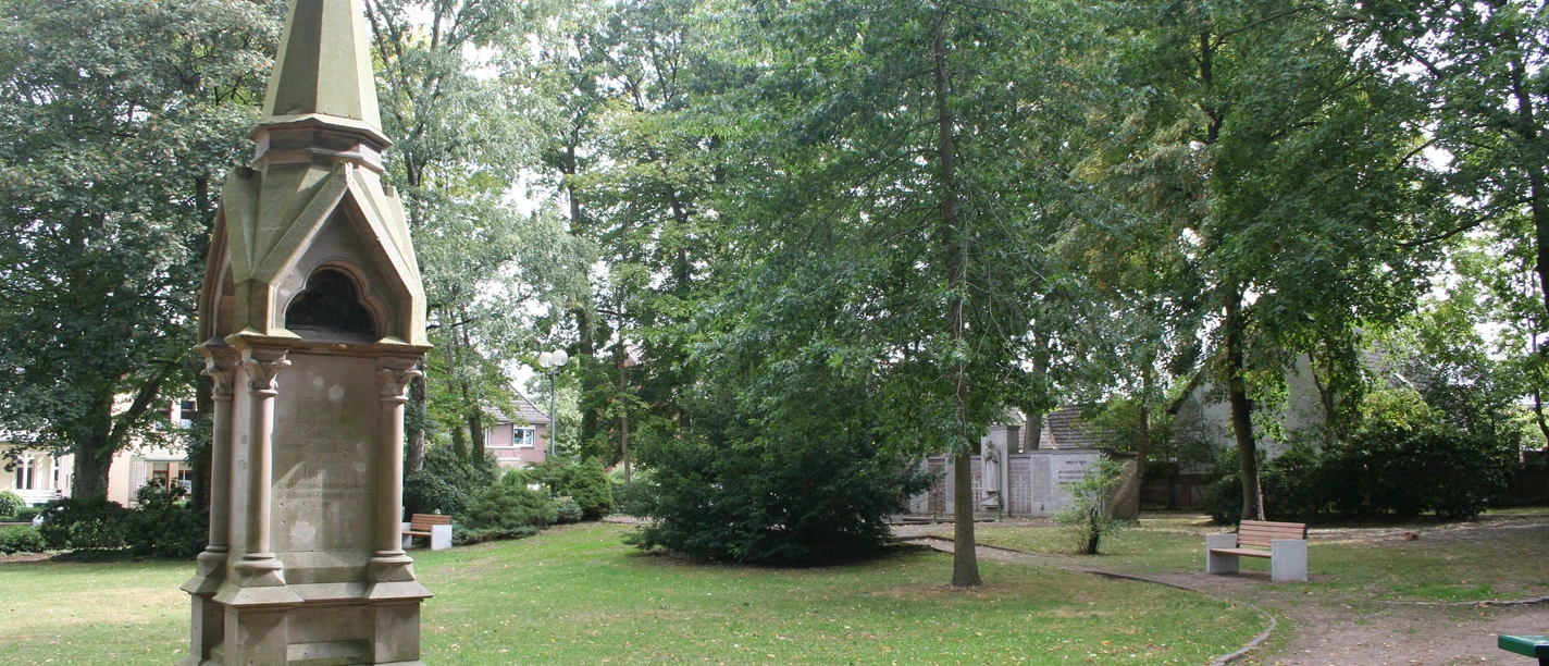 Steinernes Langensalza-Denkmal im Grünen, umgeben von Bäumen und einem gepflegten Weg.