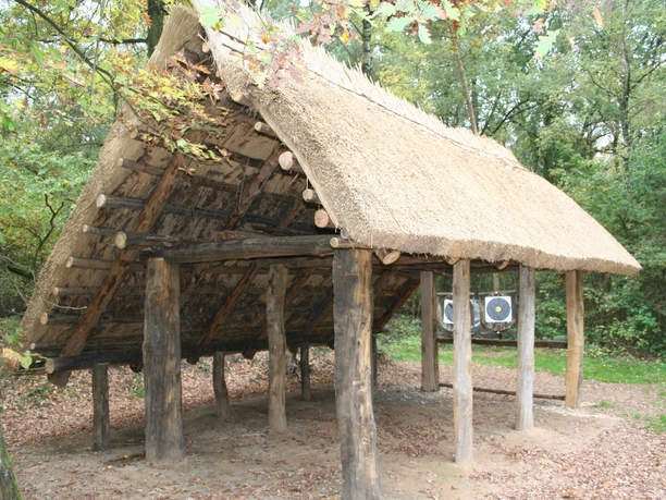 Rekonstruktion eines historischen altsächsischen Langhauses mit strohgedecktem Dach in einem Wald.