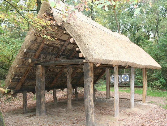 Rekonstruktion eines historischen altsächsischen Langhauses mit strohgedecktem Dach in einem Wald.