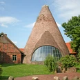 Großes, rundes Backsteingebäude der historischen Glashütte Gernheim mit Holzschindeldach und Fensterfront.