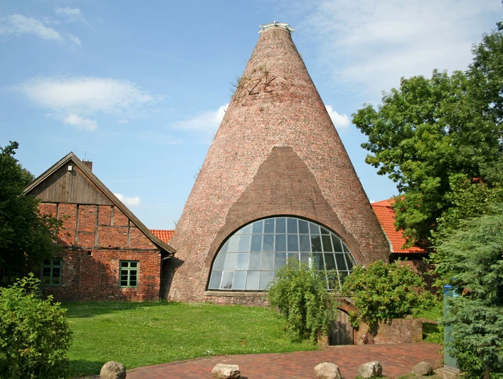 Glashütte Gernheim Großes, rundes Backsteingebäude der historischen Glashütte Gernheim mit Holzschindeldach und Fensterfront.