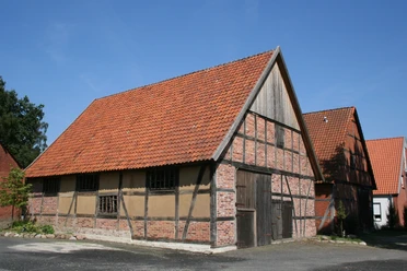 Scheunenviertel Liebenau Fachwerkhaus mit rotem Ziegeldach und Holztür in Liebenau, umgeben von Bäumen und klarer Himmel.
