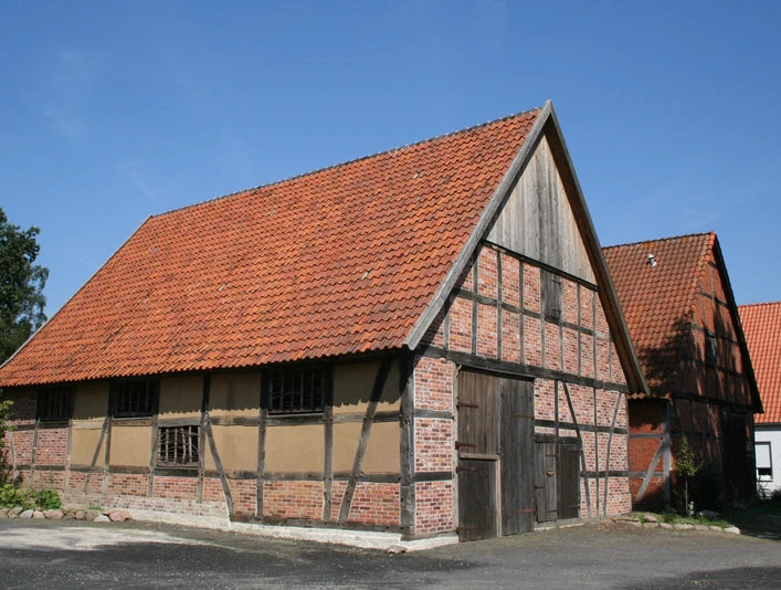 Scheunenviertel Liebenau Fachwerkhaus mit rotem Ziegeldach und Holztür in Liebenau, umgeben von Bäumen und klarer Himmel.
