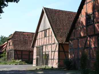 Drei historische Fachwerkscheunen mit roten Ziegeldächern stehen auf einer sonnigen, ruhigen Fläche.