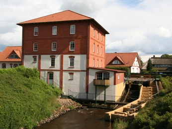 Wassermühle mit rotem Ziegelbau und Flusslauf, umgeben von grüner Landschaft und bewölktem Himmel.Watermill with red brick building and river course, surrounded by green landscape and cloudy sky.Vandmølle med rød murstensbygning og flodløb, omgivet af grønt landskab og overskyet himmel.Watermolen met rood bakstenen gebouw en rivierloop, omgeven door groen landschap en bewolkte lucht.