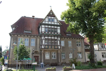 Altes Amtsgericht Petershagen Fachwerkhaus mit dekorativem Giebel, umgeben von Bäumen und Laternen, unter blauem Himmel.