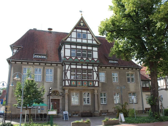 Altes Amtsgericht Petershagen Fachwerkhaus mit dekorativem Giebel, umgeben von Bäumen und Laternen, unter blauem Himmel.