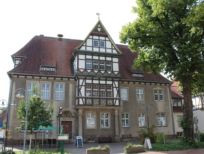 Altes Amtsgericht Petershagen Fachwerkhaus mit dekorativem Giebel, umgeben von Bäumen und Laternen, unter blauem Himmel.