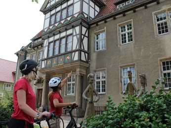 Altes Amtsgericht Petershagen Zwei Radfahrerinnen mit Helmen betrachten die kunstvoll verzierte Fachwerkfassade eines historischen Gebäudes.