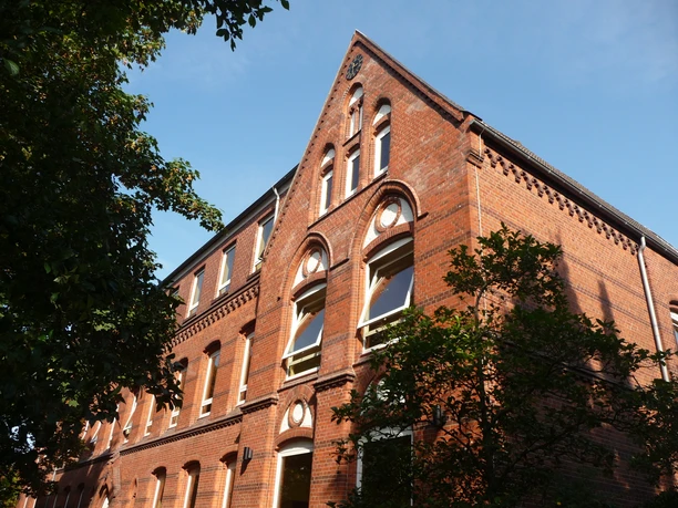 Backsteingebäude des Gymnasium am Markt mit Spitzgiebel und markanten Rundbogengiebeln im Sonnenlicht.