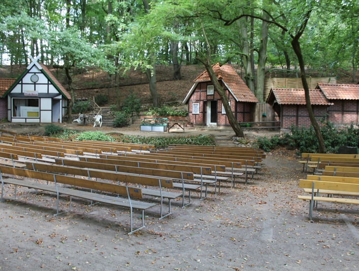 Freilichtbühne Marklohe mit Holzbänken vor rustikalen Bühnenhäusern im Wald, herbstlich umrahmt.