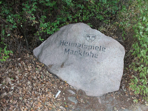 Freilichtbühne Marklohe Gedenkstein mit Inschrift "Heimspiele Marklohe" in naturbelassener Umgebung, umgeben von Blättern.