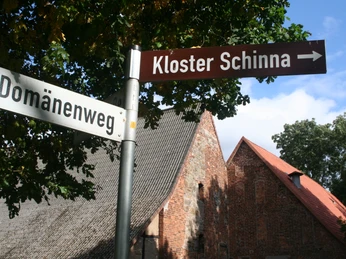 Wegweiser in der Nähe von historischem Backsteingebäude des Klosters Schinna unter blauem Himmel.Signpost near the historic brick building of the Schinna monastery under a blue sky.Skilt nær Schinna-klostrets historiske murstensbygning under en blå himmel.Wegwijzer bij het historische bakstenen gebouw van het Schinna klooster onder een blauwe hemel.