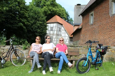 Kloster Schinna Drie mensen ontspannen op een bankje voor het historische klooster van Schinna, omringd door fietsen.