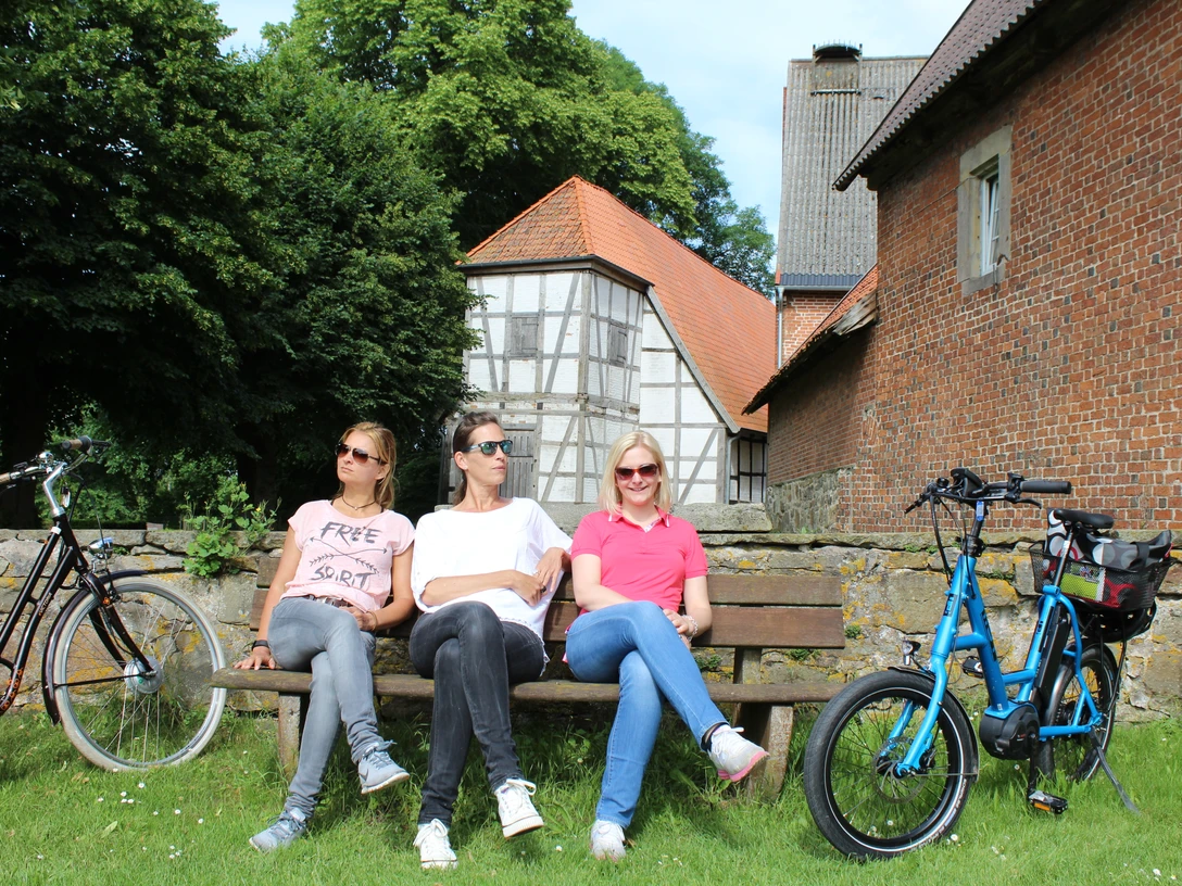 Kloster Schinna Drei Personen entspannen auf einer Bank vor dem historischen Kloster Schinna, umgeben von Fahrrädern.Three people relax on a bench in front of the historic Schinna Monastery, surrounded by bicycles.Tre personer slapper af på en bænk foran det historiske Schinna-kloster, omgivet af cykler.Drie mensen ontspannen op een bankje voor het historische klooster van Schinna, omringd door fietsen.