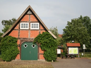Mühlenplatz Landesbergen Historisches Fachwerkgebäude mit grünem Holztor, umgeben von Bäumen und Infotafel auf dem Mühlenplatz.