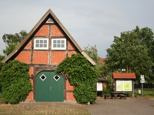 Mühlenplatz Landesbergen Historisches Fachwerkgebäude mit grünem Holztor, umgeben von Bäumen und Infotafel auf dem Mühlenplatz.