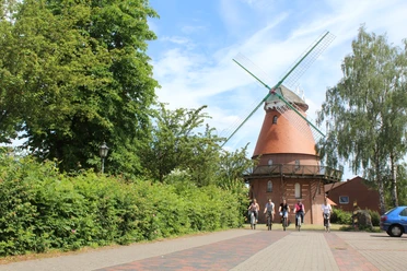 Landesberger Hochzeitsmühle Eine historische Windmühle im Grünen, von Radfahrern besucht, steht unter blauem Himmel.